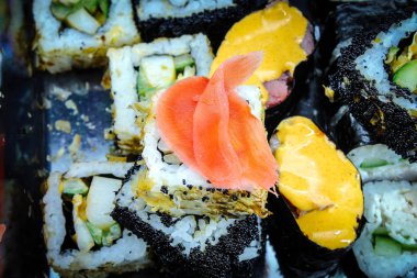 Yatay fotoğraf yakın plan yiyecekleri gösteriyor: pirinç ruloları, wasabi, zencefil. Yuvarlaklar beyaz bir tabakta yatıyor. Rolls 'un dolguları farklı.
