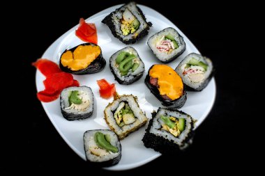 Beyaz tabağın siyah zeminindeki yatay fotoğraflarda, üzerinde taze yiyecekler var: börek, wasabi, zencefil. Ekmekler daire şeklinde dizilmiş, ekmekler farklı dolgulu.