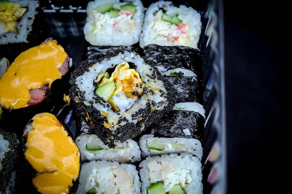 On a black background in a transparent box is a set of fresh rolls, ready to eat. The rolls are shown in close-up. Rolls have different fillings