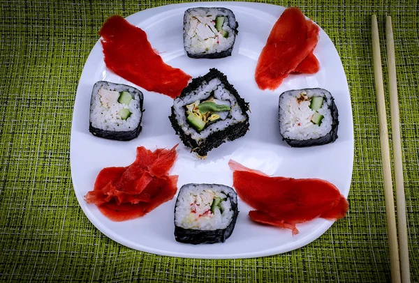 横の写真は 白いプレートの上に横たわるすぐに食べる食事を示しています 生姜の葉と5つの米ロール 近くに竹の杖 2つの部分うそ プレートは緑のテーブルクロスにあります — ストック写真