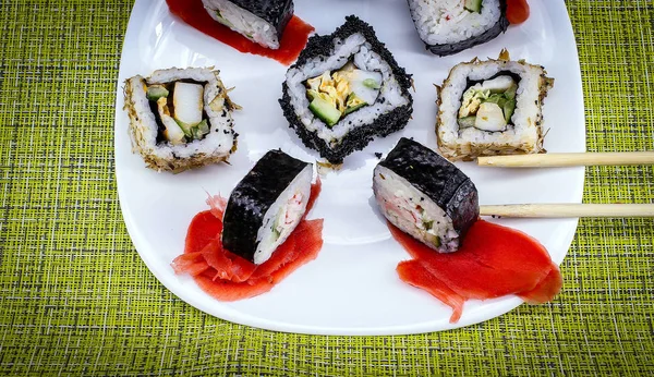 横の写真は 白いプレートの上に横たわるすぐに食べる食事を示しています 生姜の葉と5つの米ロール 近くに竹の杖 2つの部分うそ プレートは緑のテーブルクロスにあります — ストック写真