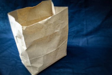 Mavi arka planda bir kese kâğıdı yerleştiriliyor, içinde ürünlerin alındığı bir kağıt paket. Paket şimdi boş ve açık.