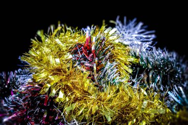 Siyah arkaplandaki yatay bir fotoğrafta, boşluk Noel 'in renkli parlak süslemeleriyle dolu. Tinsel kırmızı, gümüş, yeşil, mavi, mor, sarı