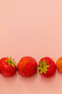 Olgun kırmızı çilekler pembe arka planda yatar.
