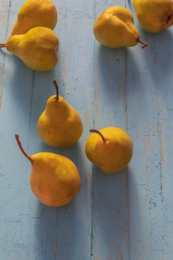 Bir armut dikey fotoğrafında. Uzun zamandır maviye boyanmış ahşap bir masanın üzerindeler. Armutlar temiz..