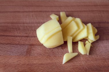 Tahtadaki yatay fotoğrafta belli ürünleri kesmek için bir patates var. Kısmen ince dilimlere bölünmüş. Patatesler çiğ, temiz.