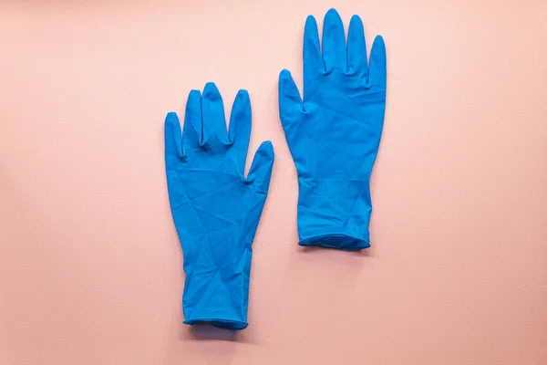 View from above on blue protective gloves. The gloves lie against a pink background. The gloves are slightly crumpled. They are sturdy, not thin, for cleaning indoors