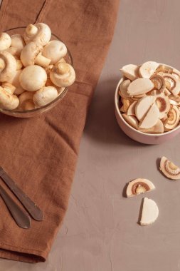 Dikey görüntü yenilebilir mantarları gösteriyor. Küçük ve beyazlar. Gelecekte çorba yapmak için marketten alınmış mantarlar. Bir tabakta, bütün mantarlar, ikinci kasede, ince doğranmış mantarlar.