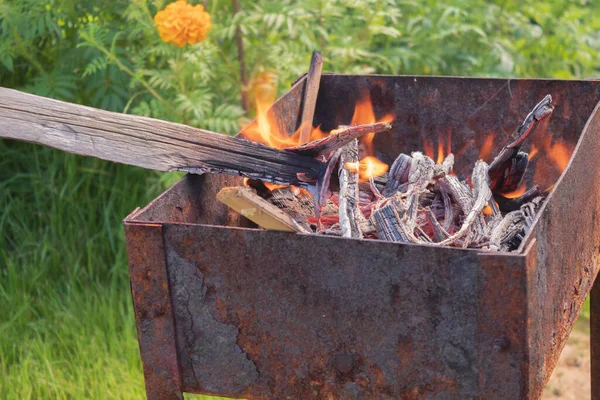 A small fire burns in an old grill on the street in the summer — Stock Photo, Image