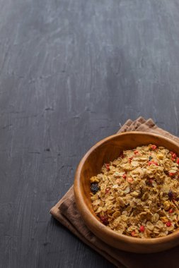 Kuru üzümlü müsli, kurumuş kızılcık ve siyah arka planda ahşap bir tabakta çilek.