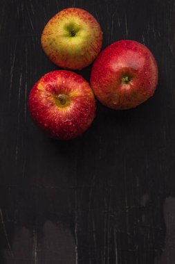 Tahta bir arka planda üç sulu elma ve su damlaları yatıyor.