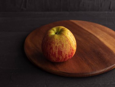 Küçük bir elma yuvarlak bir tahta kesme tahtasının üzerinde duruyor.