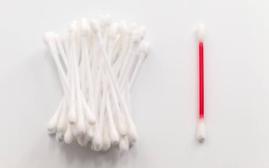 Yatay fotoğrafta, kişisel bakım ürünlerinin görüntüsü. Kenarlarında sabitlenmiş pamuklu bir çubuk. Bir çubuk kırmızı, diğeri beyaz. Tüm çubuklar beyaz bir arka planda yatıyor.