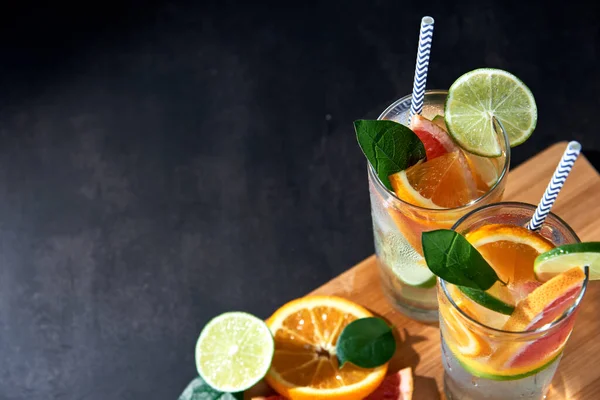 Health care, fitness, healthy nutrition diet concept. Fresh cool homemade citrus infused detox water with grapefruit, orange, lemon and lime and ice in glasses on dark background.