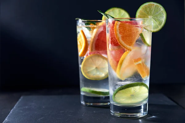 Health care, fitness, healthy nutrition diet concept. Fresh cool homemade citrus infused detox water with grapefruit, orange, lemon and lime and ice in glasses on dark background.