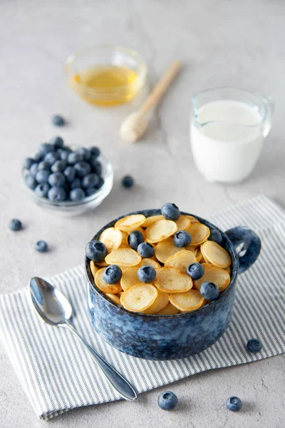 Blue Bowl of mini pancake cereal with blueberries, maple syrup and milk on concrete background. Tiny pancakes, new food trend concept. Cute healthy breakfast or snack. Recipe, menu.