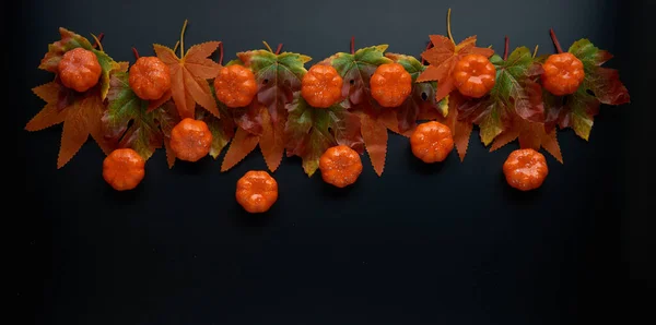 Composition of fall or autumn leaves and pumpkins on a dark background. Autumn, fall, halloween, thanksgiving day concept. Flat lay, top view, copy space..