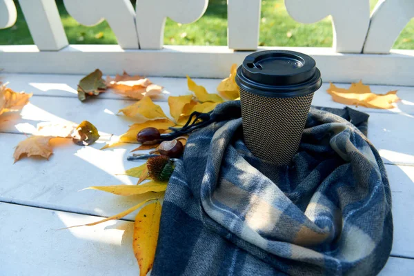 Plastic cup of coffee, autumn leaves and warm scarf on white wooden bench. Fall season, weekend, still life, leisure time and coffee break concept. Selective focus. Top view, copy space.