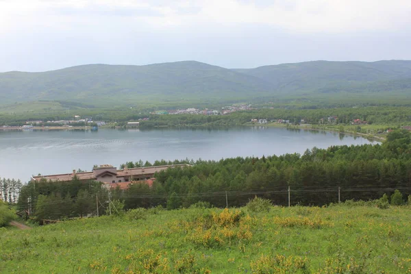 Panoramik manzara. Görkemli dağların ortasında sisli, temiz bir dağ gölü olan bir göl. Yeşil çimenler. Gölün çevresindeki daireler.
