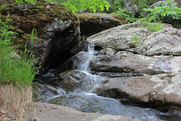 Horská řeka - malý vodopád na řece s křišťálově čistou vodou, která teče mezi šedými kameny v zeleném lese za oblačného letního dne. Velké kameny u rybníka — Stock fotografie