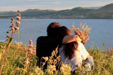 Birbirine aşık çiftler. Dağ gölünün gölünde, bir kızla birlikte bir dağda kucaklaşan bir adam. Dağların ve gölün panoramik manzarası. Gün batımı. Sevgi. Rahatla.