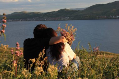 Birbirine aşık çiftler. Dağ gölünün gölünde, bir kızla birlikte bir dağda kucaklaşan bir adam. Dağların ve gölün panoramik manzarası. Gün batımı. Sevgi. Rahatla.