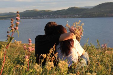 Birbirine aşık çiftler. Dağ gölünün gölünde, bir kızla birlikte bir dağda kucaklaşan bir adam. Dağların ve gölün panoramik manzarası. Gün batımı. Sevgi. Rahatla.