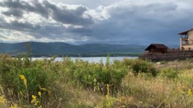 Yaz manzarası. Dramatik bir gökyüzü. Dağ Gölü. Güzel bulanık arkaplan. Arkasında ağaçlar ve dağlar olan büyük yeşil bir tarla. Arka planda dağ olan bir su kütlesi.