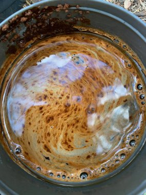 Gökyüzü bir kahve fincanına yansıyor. Bir kase yakın çekim. Köpüklü süslü kahve kalıpları.