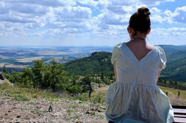Dağın tepesindeki genç bir kız yukarıdan panoramik bir manzaranın tadını çıkarıyor. Yaz mükemmel manzara