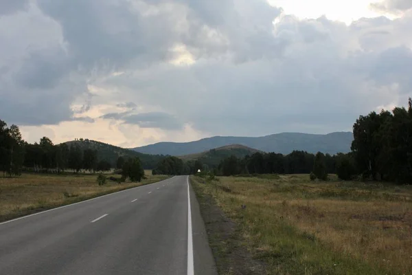 Uma estrada nas montanhas que vai muito além do horizonte ao pôr do sol — Fotografia de Stock