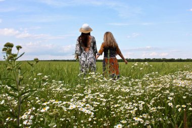 Mutlu iki kız el ele tutuşarak papatya tarlasında yürüyor...