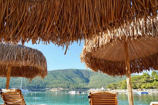 Zümrüt suyu, yatlar ve arka planda yeşil tepeler olan beyaz bir sahilde bambu şemsiyeler. Lüks Turizm Konsepti