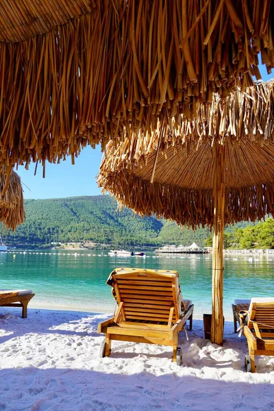 Bodrum, Türkiye - Ağustos 2020: Beyaz kum, çam ağaçları, açık mavi gökyüzü, bambu şemsiyeli plaj. Rahatla Lüks Turizm Gebeliği, Tatiller ve Yaz Konsepti