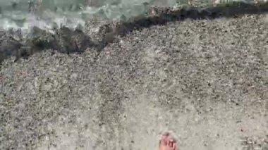 4K video. Bir kız açık zümrüt deniz sularına giriyor, kumlu tabanı görünüyor, Ege Denizi 'nin temiz tonları ve renkleri. Güzel, saf doğa çekimi.