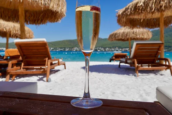 Zümrüt bir körfezde kumsalda beyaz kumların üzerinde ahududulu bir bardak şampanya. Deniz manzaralı lüks bir otel. Romantik tatil