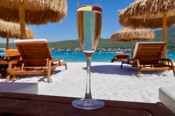 Стакан шампанського з малиною на білому піску на пляжі в смарагдовій бухті. Розкішний курорт з видом на море. Романтичний відпочинок Стокове Зображення