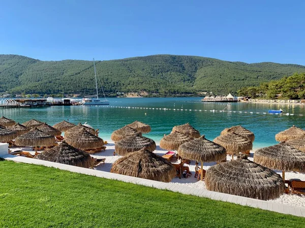 Beyaz kumlu, yeşil tepeli, kar beyazı yatlı tropikal plajda şemsiye. Lüks gebelik