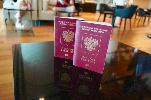 Dünya seyahatine pasaportlar. Seyahat tasarımı. Masadaki iki kırmızı pasaport havaalanı girişinde kayıt için hazır. Havaalanı salonunun arka planında iki Rus pasaportu var. — Stok fotoğraf