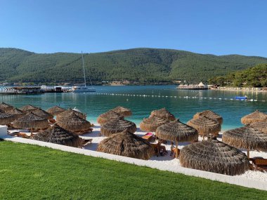 Beyaz kumlu, yeşil tepeli, kar beyazı yatlı tropikal plajda şemsiye. Lüks gebelik