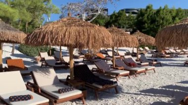 4K Emerald Lagoon, Türkiye 'deki Lujo Luxury Oteli' nin beyaz plajında kar beyazı eko yatları, güneş pansiyonları ve bambu şemsiyeleri olan ebedi yeşil tepelere bakıyor.