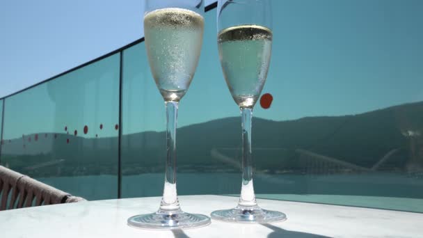 4K video Två höga glas champagne med bubblor på ett vitt bord mot en blå, festlig dryck med reflektion. — Stockvideo