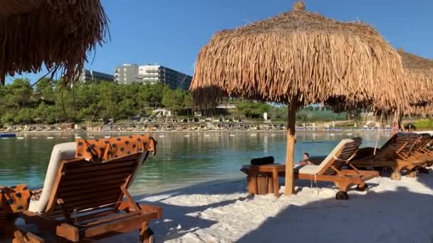 Água do mar azul-turquesa e idílica praia de areia branca em Bodrum, Turquia, vista panorâmica. Garçons caminham na praia Fundo natural para férias de verão. — Vídeo de Stock