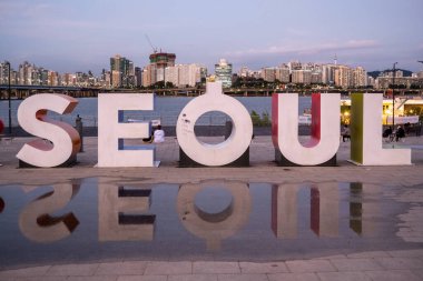 6 Ekim 2021 'de Güney Kore' nin Seul şehrinin arka planında şehir silueti olan Han nehri kıyısındaki Yeouido Parkı 'nda büyük Seul tabelası