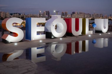 6 Ekim 2021 'de Güney Kore' nin Seul şehrinin arka planında şehir silueti olan Han nehri kıyısındaki Yeouido Parkı 'nda büyük Seul tabelası