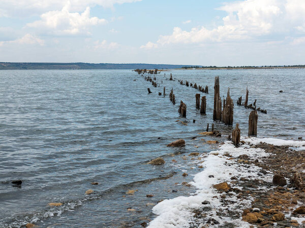 Salty estuary Kuyalnik, dead lake near Odessa, Ukraine. Wooden sticks reflected in blue water at sunny weather. 