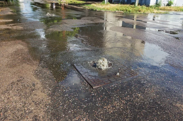 Water flows out of drainage hatch. Drainage fountain of sewage. Accident in sewage system. Dirty sewer water flows fountain on road. Drainage system for wastewater discharge does not work