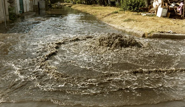 Water flows out of drainage hatch. Drainage fountain of sewage. Accident in sewage system. Dirty sewer water flows fountain on road. Drainage system for wastewater discharge does not work