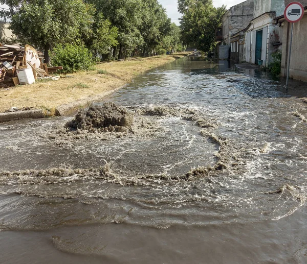 Water flows out of drainage hatch. Drainage fountain of sewage. Accident in sewage system. Dirty sewer water flows fountain on road. Drainage system for wastewater discharge does not work