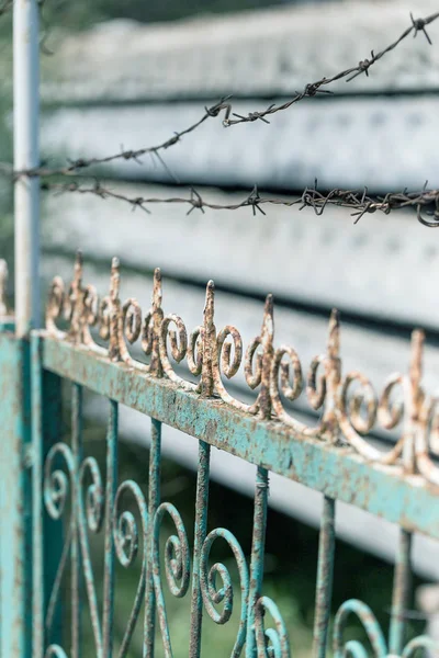 ボケ味とぼかし 錆びた古代彫刻のフェンス 緑とやり場のない背景に有刺鉄線 — ストック写真